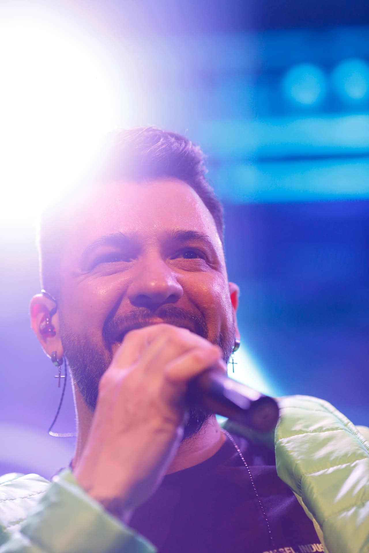 John Blanc sorrindo enquanto canta, com luz de palco ao fundo